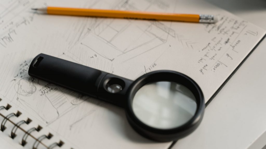 black magnifying glass beside yellow pencil